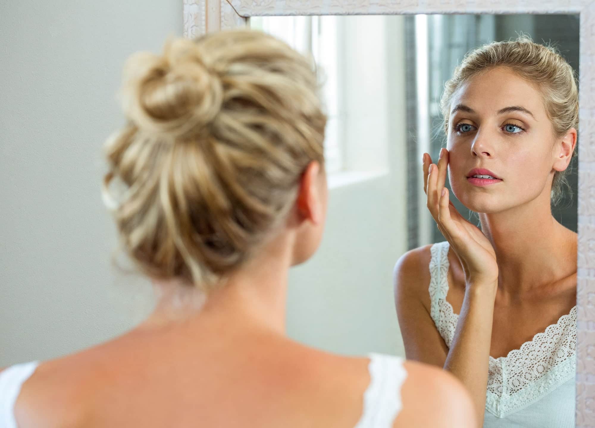 Woman looking in mirror touching face